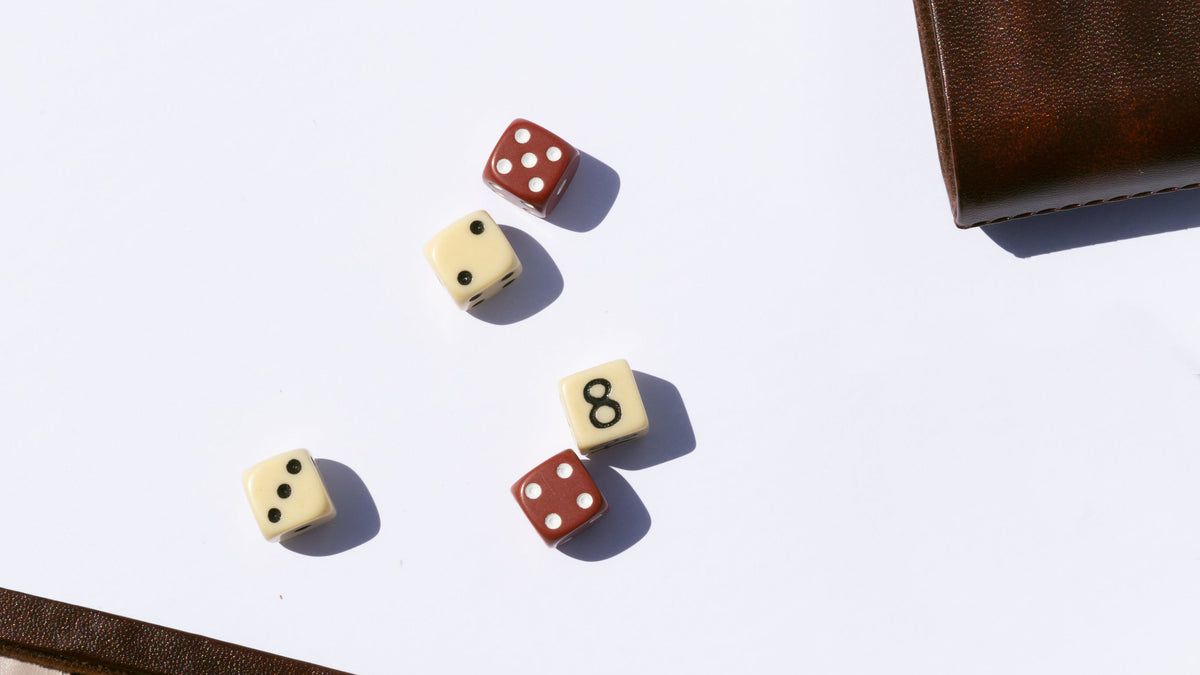 Four small dice with red and cream faces scattered on a white surface, with a brown leather corner visible in the top-right and bottom-left.